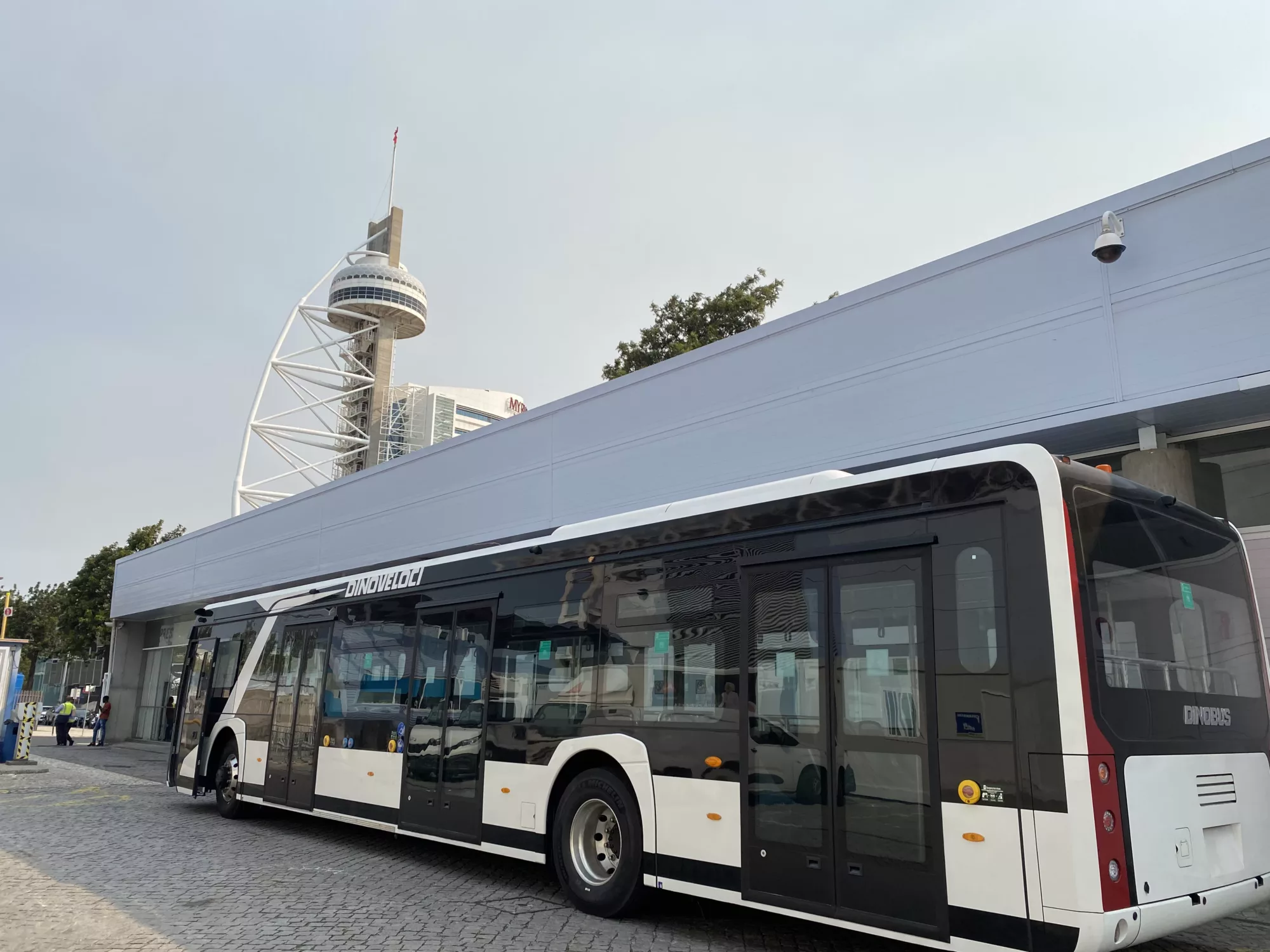 A cost effective battery electric bus on a tarmac in front of a tower